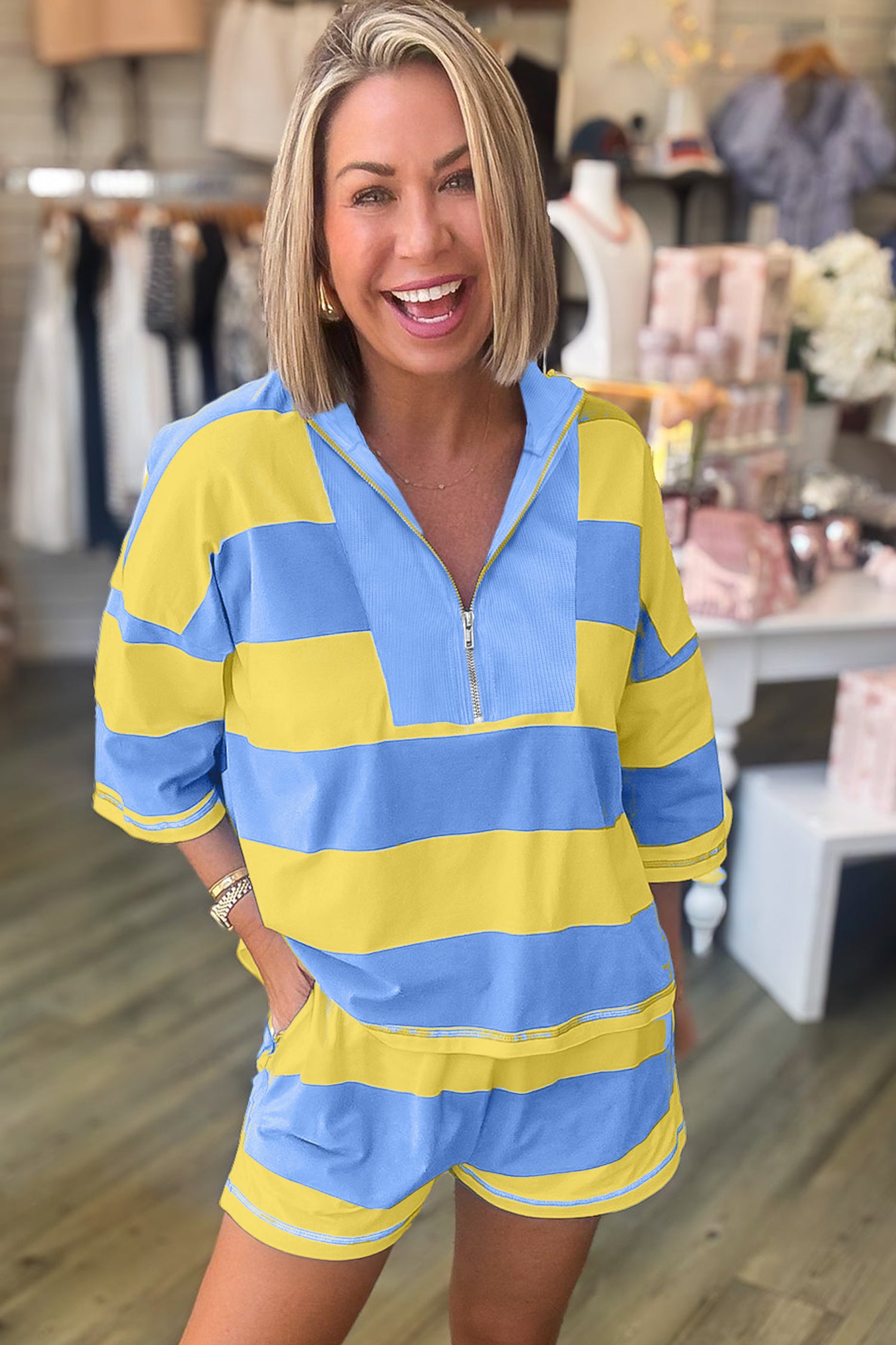 Mulher sorridente vestindo o Pink Seam Detail Half Zip Tee Casual Shorts 2pcs Set com riscas largas azul e amarelo, em ambiente descontraído de loja, simbolizando suplementos premium naturais para energia, vitalidade e saúde cognitiva.