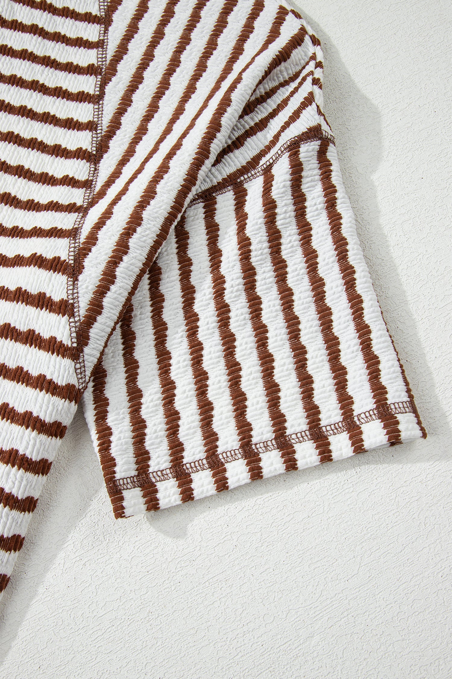 Detalhe da manga do Apricot Stripe Textured Knit Split Hem Half Sleeve Loose Top com padrão listrado em tons de bege e castanho, tecido texturizado, destacando acabamento de alta qualidade e conforto para uso diário.