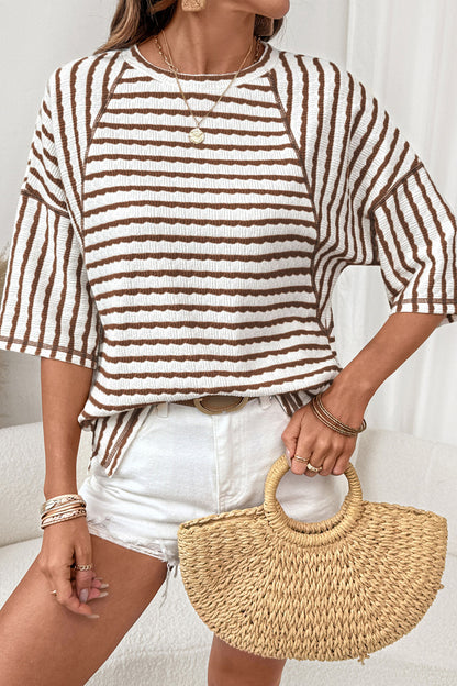 Mulher vestindo Apricot Stripe Textured Knit Split Hem Half Sleeve Loose Top com listras marrons sobre fundo branco, usando acessórios dourados e segurando bolsa de palha, promovendo suplementos premium naturais para energia, vitalidade e saúde cognitiva em Portugal.