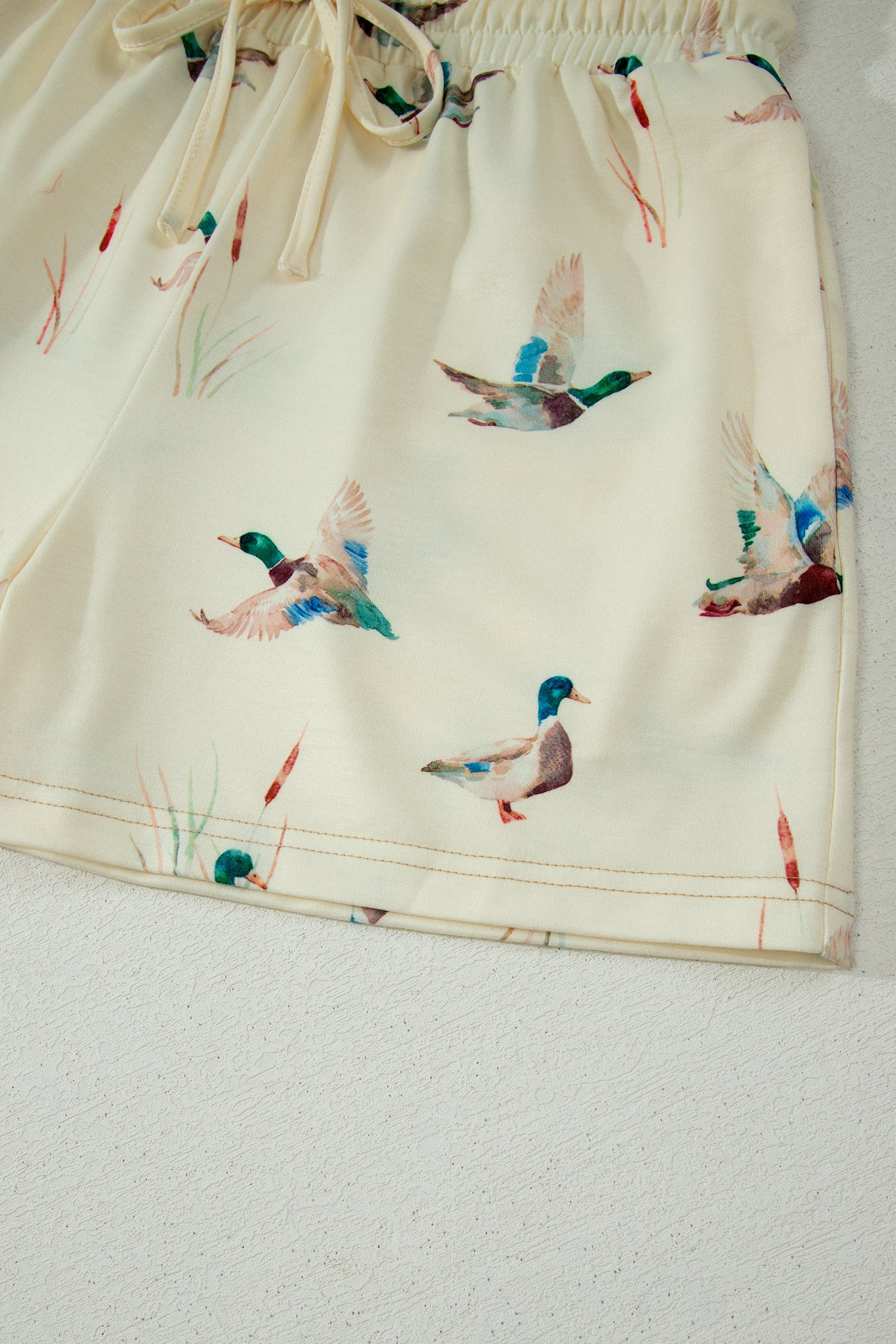 Detalhe da Beige Mallard Duck Print Oversized Tee Drawstring Short Set em tecido bege com estampa de patos voando e acabamento com cordão ajustável na cintura, transmitindo conforto e estilo casual.