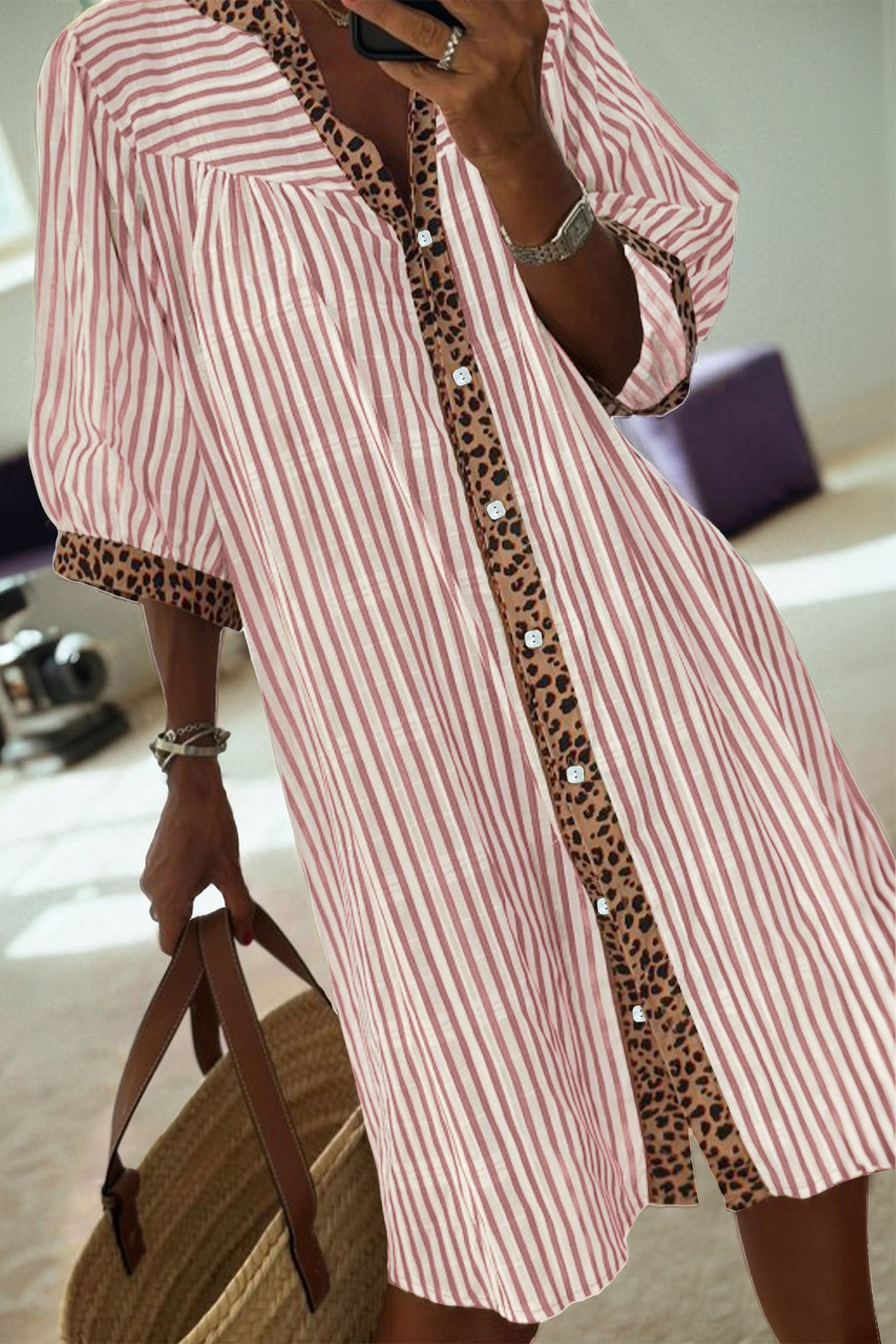 Mulher vestindo Khaki Stripe Square Button Leopard Trim Loose Bracelet Sleeve Shirt Dress com padrão de riscas khaki e detalhes em padrão de leopardo, segurando bolsa de palha em ambiente iluminado, associando estilo casual e conforto.
