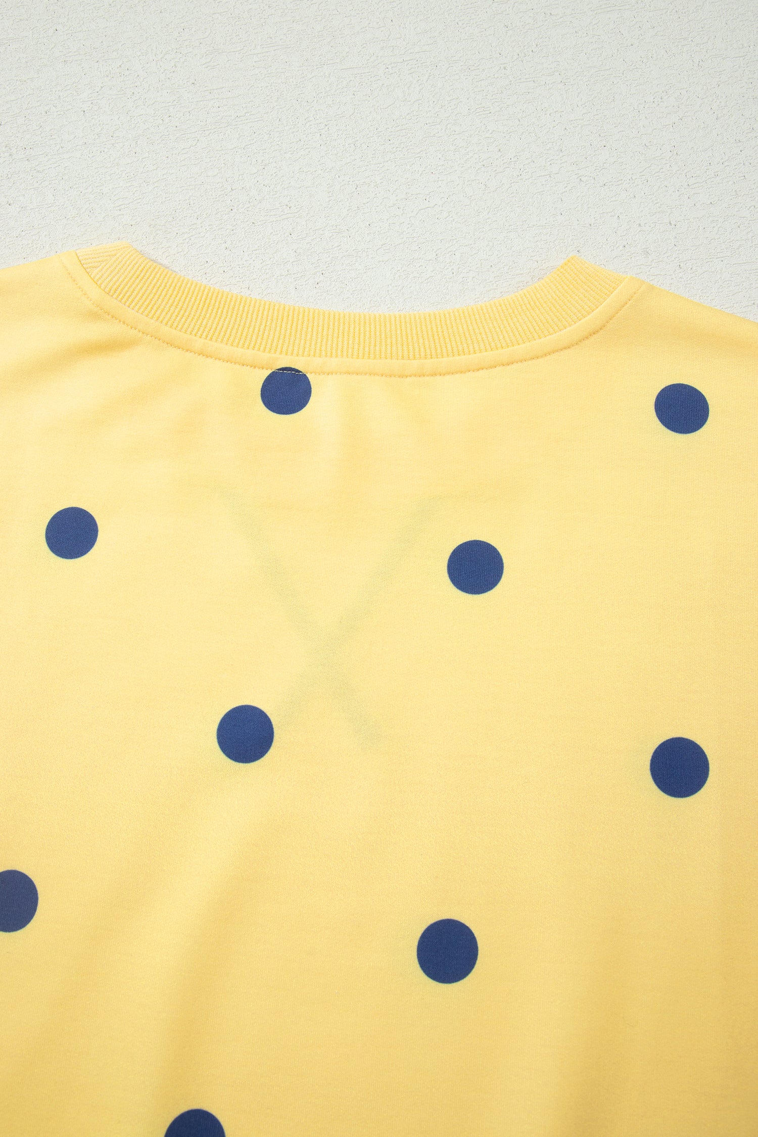 Detalhe das costas da Yellow Polka Dot Print Crossed Seam Detail Oversize Tee, com padrão amarelo e bolinhas azuis, destacando costura cruzada e estilo oversize, ideal para conforto e bem-estar natural.
