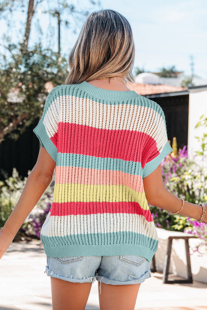 Mulher vista por trás usando Green Stripe Color Block Hollow Out Knit Short Sleeve Sweater com listras coloridas e calções de ganga, em ambiente exterior ensolarado, transmitindo estilo casual e fresco.