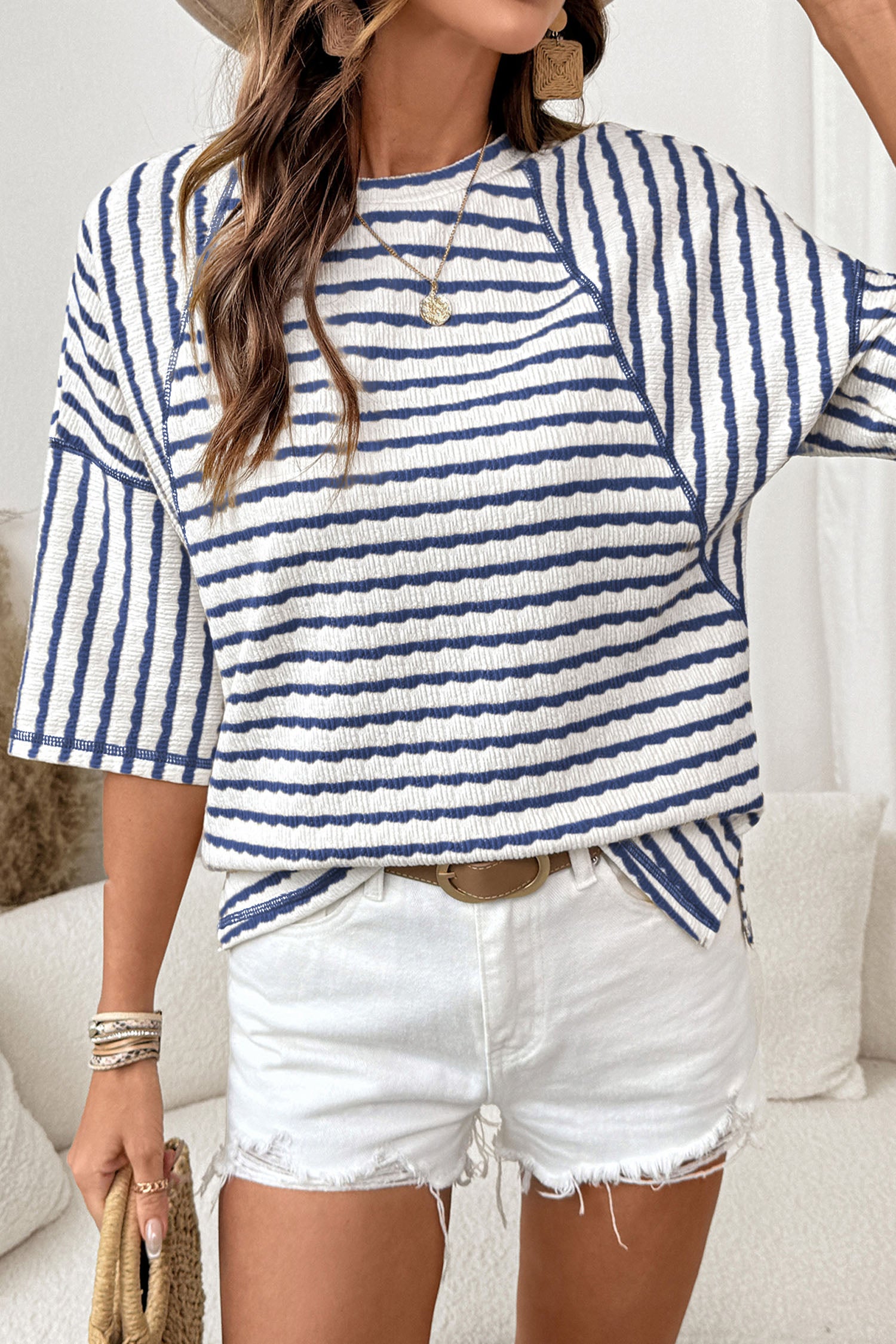 Modelo feminina usando Apricot Stripe Textured Knit Split Hem Half Sleeve Loose Top com padrão listrado azul e branco, complementado por acessórios em tom neutro e shorts brancos, transmitindo estilo casual e conforto.
