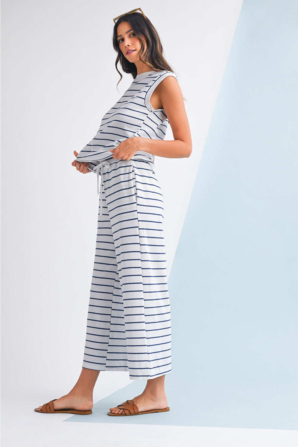 Mulher vestindo o conjunto Sail Blue Casual Striped Tee and Wide Leg Pants Set, composto por blusa sem mangas e calças largas de riscas azuis, num ambiente minimalista e sereno.
