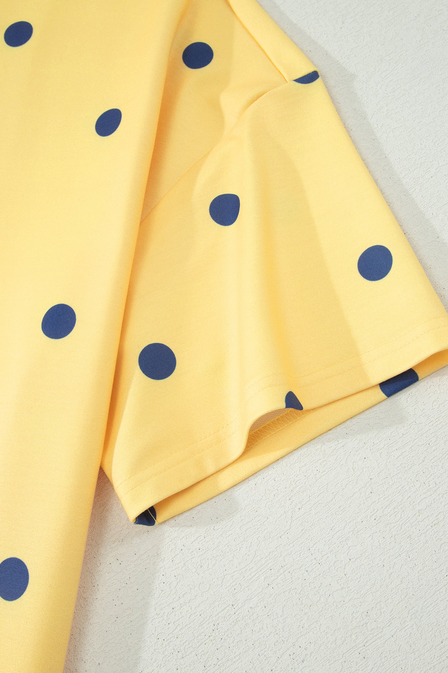 Detalhe da manga da Yellow Polka Dot Print Crossed Seam Detail Oversize Tee em tecido amarelo com estampa de bolinhas azuis, transmitindo estilo e vitalidade de suplementos premium naturais para energia, vitalidade e saúde cognitiva.