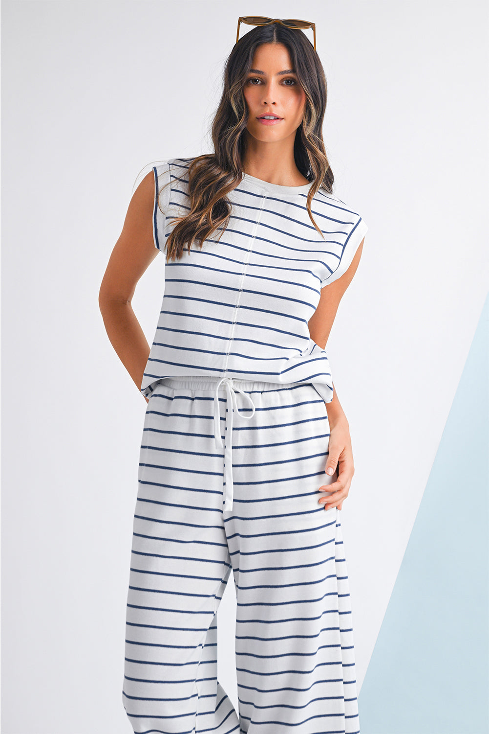 Mulher com cabelo ondulado usando o conjunto Sail Blue Casual Striped Tee and Wide Leg Pants Set branco com riscas azuis, em pose descontraída para promocionar suplementos premium naturais para energia, vitalidade e saúde cognitiva.