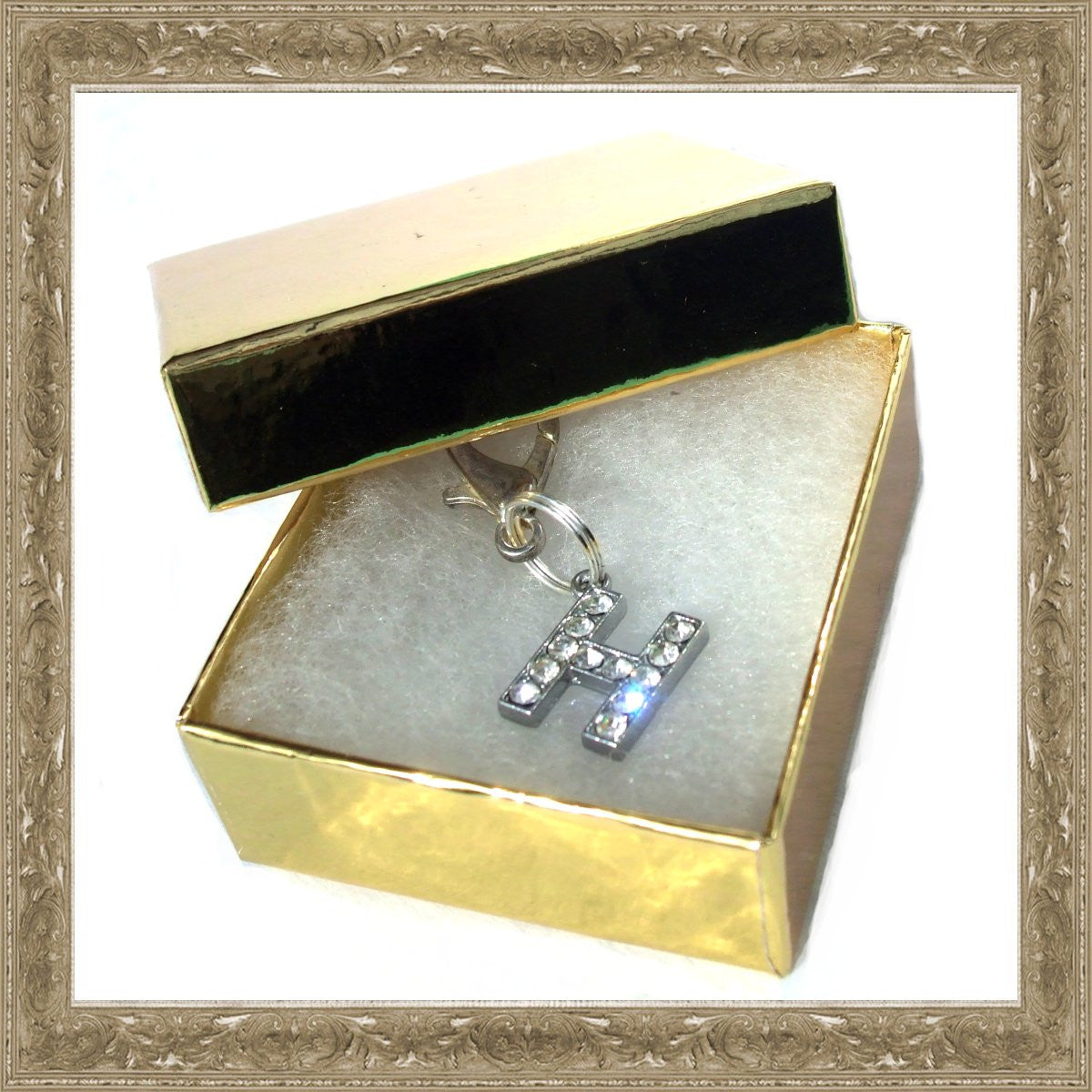 Caixa dourada aberta com pendente em forma de letra H cravejado de cristais brilhantes, parte dos A-Z Crystal Letter Pet Charms, suplementos premium naturais para energia, vitalidade e saúde cognitiva.